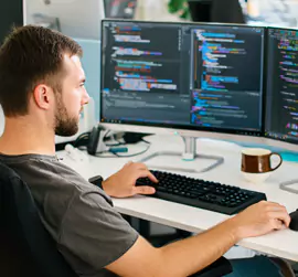 Person, die an einer Dual-Monitor-Workstation in einem modernen Büro programmiert.